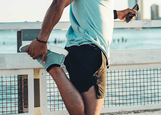 Hardloper doet dynamische warming-up oefening langs een parkpad